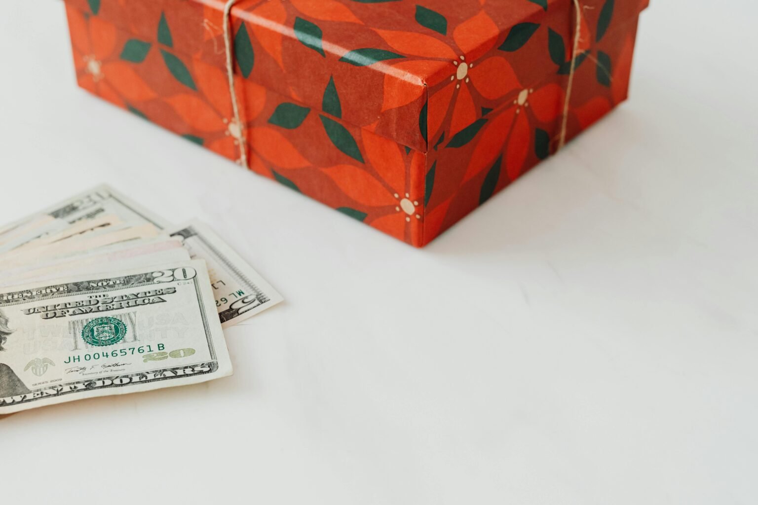 Red wrapped gift box alongside U.S. dollar banknotes on a white background.
